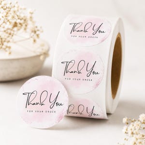 May include: A roll of circular adhesive labels featuring a soft pink watercolor background and the black text Thank You FOR YOUR ORDER. The stickers are presented on a white backing paper, with one individual sticker detached in the foreground.