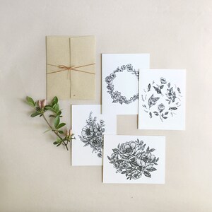 May include: Set of four blank greeting cards with black and white floral illustrations. The cards feature a wreath, a bouquet, and two arrangements of flowers.