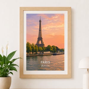 Peut inclure: Une affiche encadrée représentant la tour Eiffel à Paris, France, sous un ciel au coucher du soleil aux teintes orange et violettes. L'image montre des arbres verts le long d'une rive et un bateau sur l'eau. Le texte PARIS France est inscrit.
