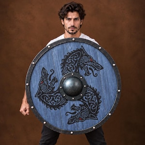 Peut inclure: Un bouclier circulaire en bois avec une finition bleue patinée et un umbo central en métal sombre. La surface est ornée de trois têtes de loup noires dans un motif de nœuds stylisé, rehaussé de petits détails rouges. Un bord en métal sombre.