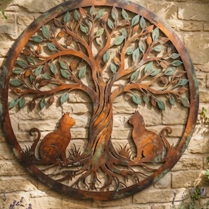 May include: A circular metal wall art piece featuring a tree with a twisted trunk and branches extending to the outer frame. Two cat silhouettes sit at the base of the tree. The metal has a weathered copper and bronze finish with green patina.
