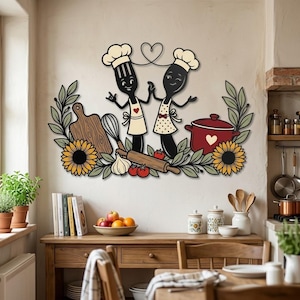 Può includere: Una decorazione da parete con una forchetta e un cucchiaio a cartone animato con cappelli da chef, circondati da un tagliere in legno, un mattarello, una pentola rossa, aglio, pomodori, girasoli e foglie verdi, con un cuore sopra le posate.