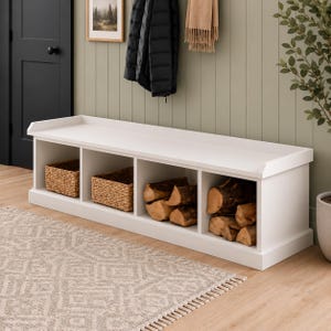 May include: A white wooden storage bench featuring four open cubby compartments. The two left cubbies contain woven wicker baskets, while the two right cubbies are filled with stacked pieces of natural brown firewood logs for storage.