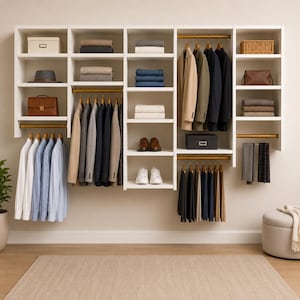 May include: A white wall-mounted wardrobe storage system comprising various shelves, hanging rails, and compartments. The unit contains folded jumpers, hanging blazers, shirts, trousers, shoes, a hat, and several storage boxes for organisation.