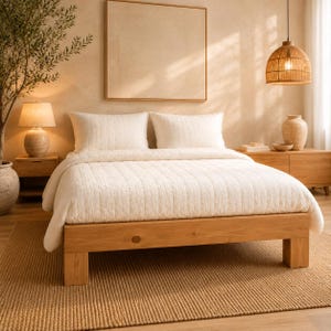 May include: A light-coloured wooden bed frame with a textured white quilt and two matching pillows. The bed is positioned in a room with a woven rug, a wooden nightstand with a lamp, a wooden dresser with a ceramic vase, and a hanging woven pendant light.