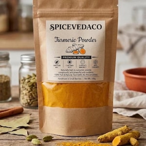 Puede incluir: Una bolsa de papel marrón de cúrcuma en polvo SPICEVEDACO con una ventana transparente que muestra polvo amarillo brillante. La etiqueta incluye una ilustración de raíz de cúrcuma, un peso neto de 100g y detalles de 100% puro y natural.