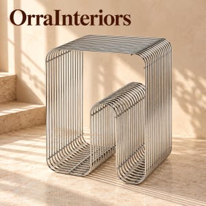 May include: A chrome side table featuring a series of parallel metal rods bent into a continuous, open-ended rectangular frame with a central curved support. The text OrraInteriors is visible in the upper left corner of the image.