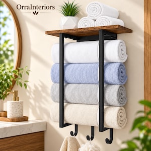 May include: A wall-mounted towel rack with a dark brown wooden shelf and a black metal frame. The rack holds four rolled towels in white, light blue, gray, and beige. Three black metal hooks hang from the bottom, holding two small cloths.