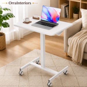 May include: A white adjustable height rolling laptop desk with a single central support column and four caster wheels. The rectangular tabletop holds a silver laptop, a white ceramic mug on a wooden coaster, and a small wooden desk calendar.