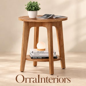 May include: A round wooden side table with four legs and a lower shelf. On the top surface sits a white potted plant and an open book. On the lower shelf, a stack of three books is topped with a small, spherical, glowing white lamp.