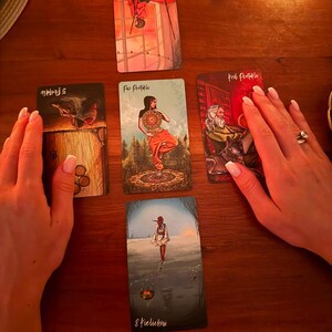 May include: Five tarot cards arranged in a cross pattern on a wooden surface. The cards include the Two of Wands, Five of Pentacles, Page of Pentacles, King of Pentacles, and Eight of Cups, featuring various illustrations of figures and symbols.
