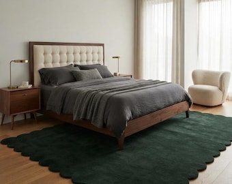 May include: A large, rectangular area rug in a deep forest green color featuring a scalloped edge design. The rug is made of a plush, textured material and is positioned on a light-colored wooden floor beneath a wooden bed frame.