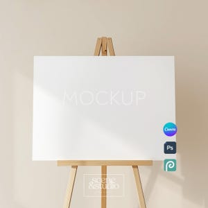 May include: A blank white rectangular sign mounted on a light brown wooden tripod easel. The sign features the word MOCKUP in light gray text. Three small circular icons for Canva, Photoshop, and a logo are visible on the right side of the sign.
