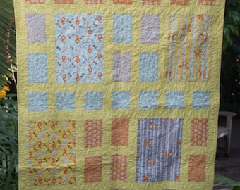 Puede incluir: Una colcha amarilla con un diseño de patchwork que presenta varios patrones en tonos de amarillo, naranja y azul. La colcha está compuesta por cuadrados y rectángulos, y los patrones incluyen diseños florales, geométricos y abstractos.