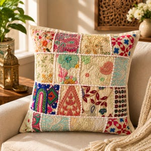 Può includere: Un cuscino quadrato caratterizzato da un design patchwork di quadrati di tessuto ricamati in crema, rosa, verde, blu e rosso. La superficie presenta intricati motivi floreali, paisley e geometrici con cuciture bianche visibili tra ogni sezione.