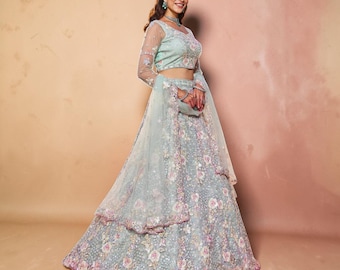 May include: A light mint green lehenga choli set featuring intricate floral embroidery in shades of pink and white. The ensemble includes a long-sleeved blouse, a voluminous floor-length skirt, and a matching sheer dupatta, all adorned with delicate sequin detailing throughout the fabric.