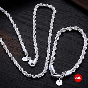Può includere: Una collana a catena ritorta e un bracciale a catena ritorta abbinato di colore argento, entrambi dotati di chiusura a moschettone e di una piccola targhetta rotonda con impresso 925. I gioielli presentano un design intrecciato e testurizzato.