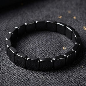以下が含まれることがあります： 滑らかで光沢のある黒い正方形のビーズで構成されたストレッチブレスレット。ビーズは連続した円形のループ状に配置されており、光を反射する表面が特徴で、全体的に均一で磨き上げられた外観を作り出しています。