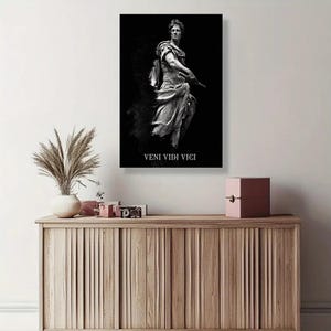 May include: A rectangular wall art print featuring a black and white depiction of a classical Roman statue of a figure in draped robes and armor. The text VENI VIDI VICI is printed in white capital letters at the bottom of the dark background.