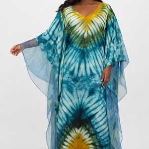May include: A floor-length kaftan dress featuring a tie-dye pattern in shades of teal, dark blue, and mustard yellow. The garment has a V-neckline, wide flowing sleeves, and a matching headband, all crafted from a lightweight, semi-sheer fabric.