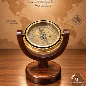 May include: A brass compass with a circular face and directional markings, mounted on a dark brown wooden gimbal and circular base. The compass features a central needle and cardinal points. Text on the image includes Craftedheritage19.