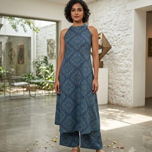 Könnte beinhalten: Ein ärmelloses blaues Tunikakleid mit einem sich wiederholenden geometrischen Rautenmuster in Hellblau und Weiß, kombiniert mit einer passenden weiten Hose. Das Outfit besteht aus gemustertem Stoff mit hohem Ausschnitt und lockerer Passform.