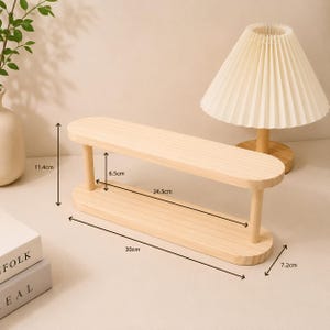 May include: A light-colored wooden two-tier display shelf with rounded ends and four cylindrical supports. The shelf measures 30 cm in total length, 7.2 cm in width, and 11.4 cm in total height, with a 6.5 cm clearance between the two tiers.