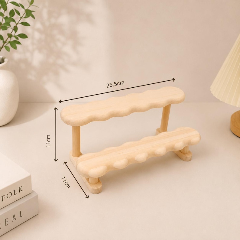 May include: A light-colored wooden two-tier display stand with scalloped edges on the shelves. The stand features vertical supports and measures 25.5 cm in length, 11 cm in height, and 11 cm in depth as indicated by the visible dimension lines.