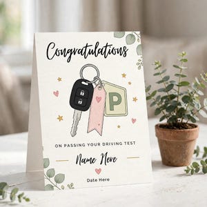 Peut inclure: Une carte de vœux avec le texte Congratulations on passing your driving test, Name Here et Date Here. Le design présente une illustration d'une clé de voiture noire, une étiquette rose et une étiquette vert clair avec la lettre P, entourées de petites étoiles, de cœurs et de feuilles vertes.