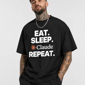 Peut inclure: Un t-shirt noir à manches courtes avec le texte blanc EAT. SLEEP. suivi d'une icône d'étoile orange, du mot Claude, et du mot REPEAT. en lettres capitales blanches. Le t-shirt présente une encolure ronde et une coupe décontractée.