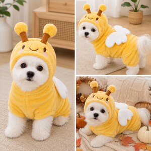 May include: A plush yellow bee costume for a small dog, featuring a hood with two brown antennae, a smiling face embroidered on the front, and white fabric wings attached to the back. The soft, fuzzy garment covers the torso and head.