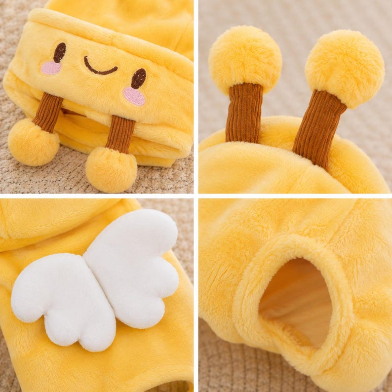 May include: A bright yellow plush hat featuring a smiling face with pink cheeks, two brown ribbed antennae topped with yellow pom-poms, and a pair of white plush wings attached to the side. The soft fabric has a fuzzy texture throughout.