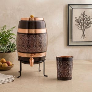 May include: A barrel-shaped water dispenser and a matching tumbler, both featuring a dark brown finish with intricate copper-coloured floral patterns. The dispenser has a copper lid with a gold knob, a copper spigot, and a black metal stand.