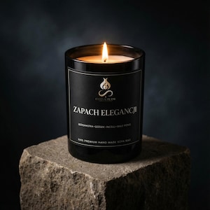 Könnte beinhalten: Eine schwarze Glaskerze mit brennendem Docht und einem Etikett mit dem Text ETERNAL FLAME, ZAPACH ELEGANCJI, BERGAMOTKA, GOŹDZIK, PACZULI, BIAŁE PIŻMO und 100% PREMIUM HAND MADE SOYA WAX. Die Kerze strahlt ein warmes orangefarbenes Licht aus.