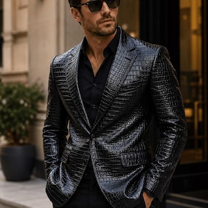 May include: A black blazer with a glossy, textured crocodile skin pattern, featuring a notched lapel, two front flap pockets, and a single button closure, worn over a solid black button-down shirt and dark sunglasses.