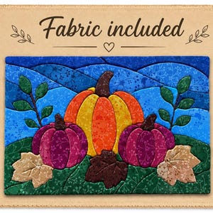 May include: A fabric quilt block featuring a central orange and yellow pumpkin flanked by two smaller purple pumpkins. The scene includes green foliage, brown and tan leaves, and a blue rolling hill background. The text Fabric included is printed above.