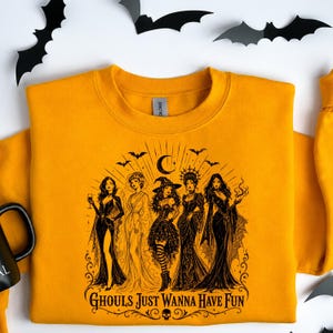 A mustard yellow crewneck sweatshirt laid flat on a white background with a black gothic witch design and paper bats.