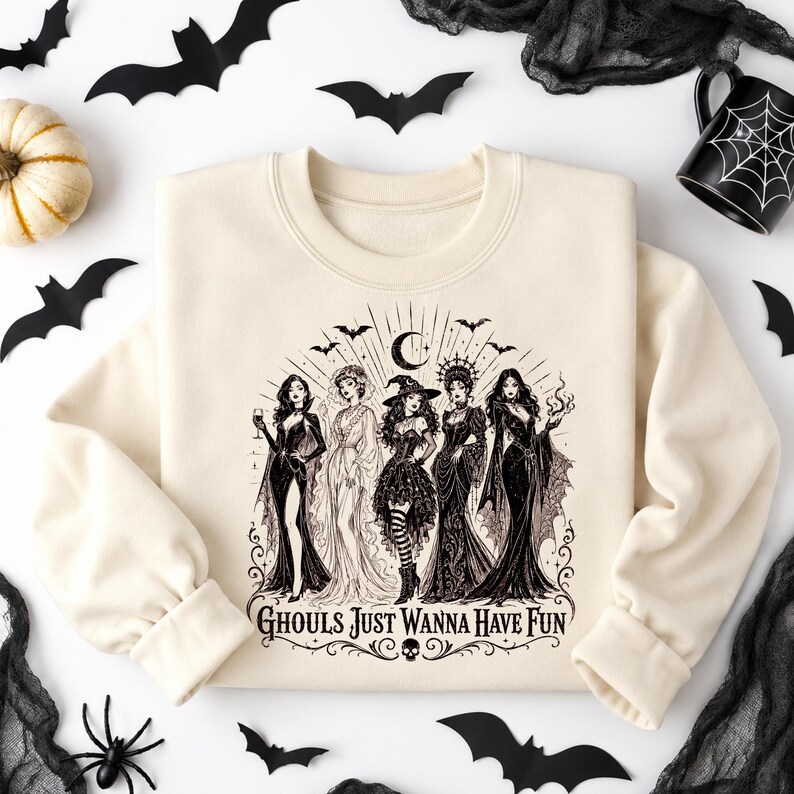 A cream-colored crewneck sweatshirt centered on a white background with a black witch coven graphic and Halloween props.