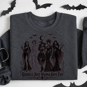 A dark charcoal gray crewneck sweatshirt featuring a dark red or black witch illustration with the text Ghouls Just Wanna Have Fun.