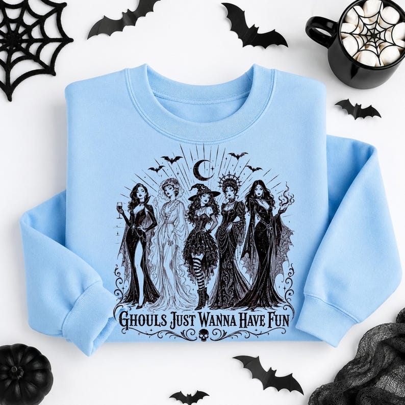 A light blue crewneck sweatshirt featuring a black graphic of witches and bats on a white background with a coffee mug and spiderweb.