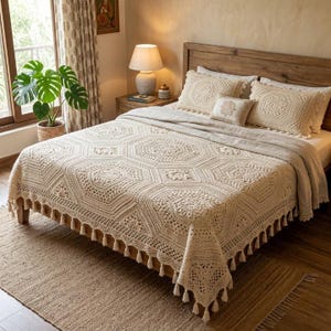 May include: A cream-colored crochet bedspread with a geometric pattern and tassel fringe edges, paired with two matching rectangular crochet pillows and one smaller square crochet pillow, all resting on a wooden bed frame with a headboard.