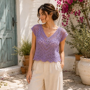 Può includere: Un top a maniche corte color lavanda caratterizzato da un intricato motivo a uncinetto traforato con scollo a V e orlo smerlato. Il capo è abbinato a pantaloni ampi color beige chiaro, creando un completo coordinato dalla finitura testurizzata.