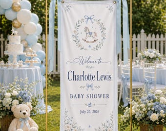May include: A vertical white banner on a gold metal stand featuring a blue rocking horse illustration, a floral wreath, and the text Welcome to Charlotte Lewis BABY SHOWER July 20, 2026. The banner is decorated with light blue satin ribbons.