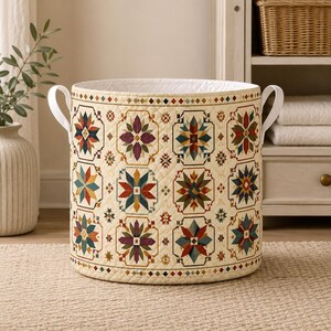 May include: A cylindrical quilted storage basket featuring a cream-colored base with a repeating geometric star pattern in shades of red, blue, green, and purple. The basket includes two white side handles and a white interior lining.