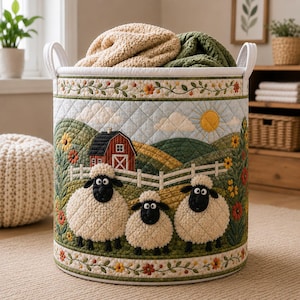 May include: A cylindrical quilted fabric storage basket featuring a farm scene with three sheep, a red barn, green hills, and a yellow sun. The basket has white handles and a floral border pattern at the top and bottom, filled with two blankets.