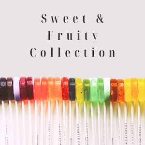 May include: A collection of colorful lollipops on white sticks. The lollipops are arranged in a row, showcasing a variety of colors including purple, red, orange, green, and yellow. The text "Sweet & Fruity Collection" is displayed above the lollipops.