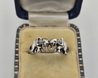 Puede incluir: Un anillo de plata con dos figuras de elefantes enfrentadas, colocado dentro de un joyero azul oscuro forrado de terciopelo con el texto Manufacturing Jewellers 28 & 30, ROSE STREET (EAST), EDINBURGH impreso en la tapa interior.