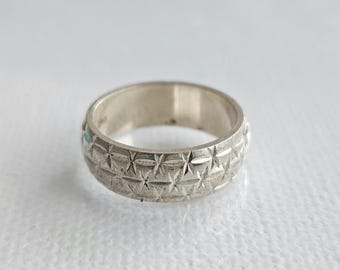 Puede incluir: Un anillo de metal plateado que presenta un patrón de estrellas grabado y repetitivo alrededor de toda la banda exterior. El anillo tiene una superficie interior lisa y pulida y un acabado exterior texturizado con múltiples detalles en forma de estrella.