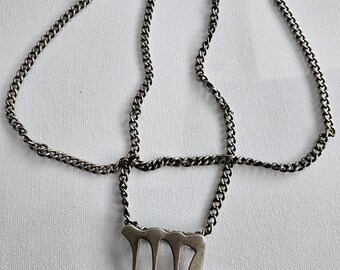 Pode incluir: Um colar de metal prateado com uma corrente de elos e um pingente em forma do símbolo do zodíaco Virgem. O pingente tem um acabamento fosco liso e está preso à corrente em dois pontos, criando uma aparência estruturada e geométrica.