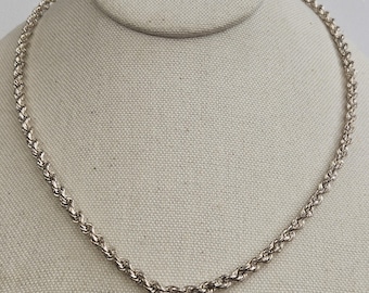 Pode incluir: Um colar de corrente tipo corda em tom prateado com um design de metal torcido e texturizado. A corrente consiste em elos interconectados que criam um padrão em espiral contínuo ao longo de todo o comprimento da peça de joalharia.